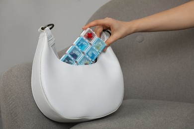 Woman putting plastic box with pills into bag on sofa indoors, closeup