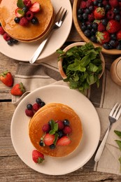 Tasty pancakes with fresh berries and mint on wooden table, flat lay