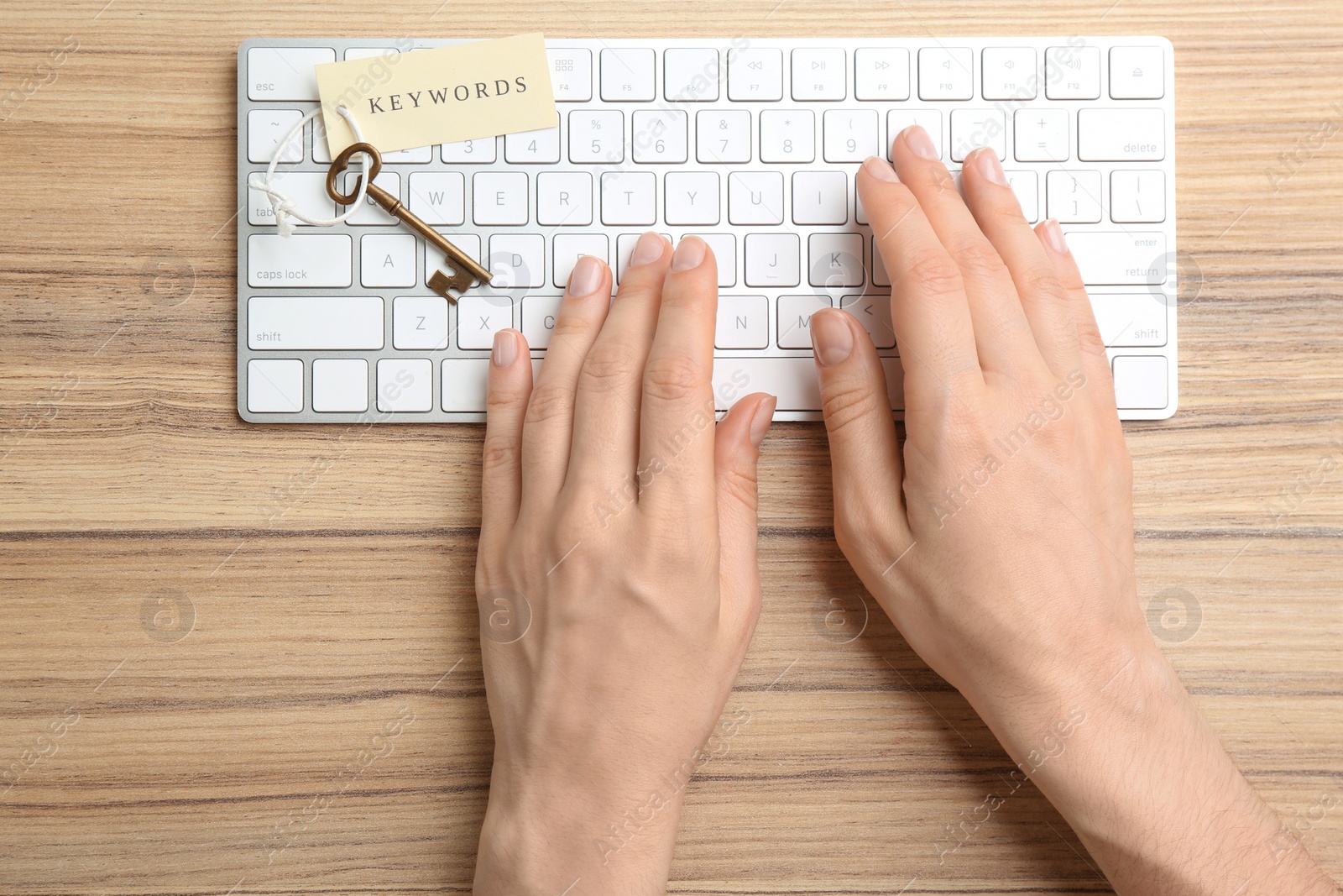 Photo of Woman typing on keyboard at wooden table, top view. Keyword concept