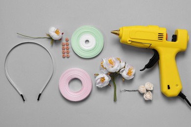 Hot glue gun, plastic headband and handicraft materials on grey background, flat lay