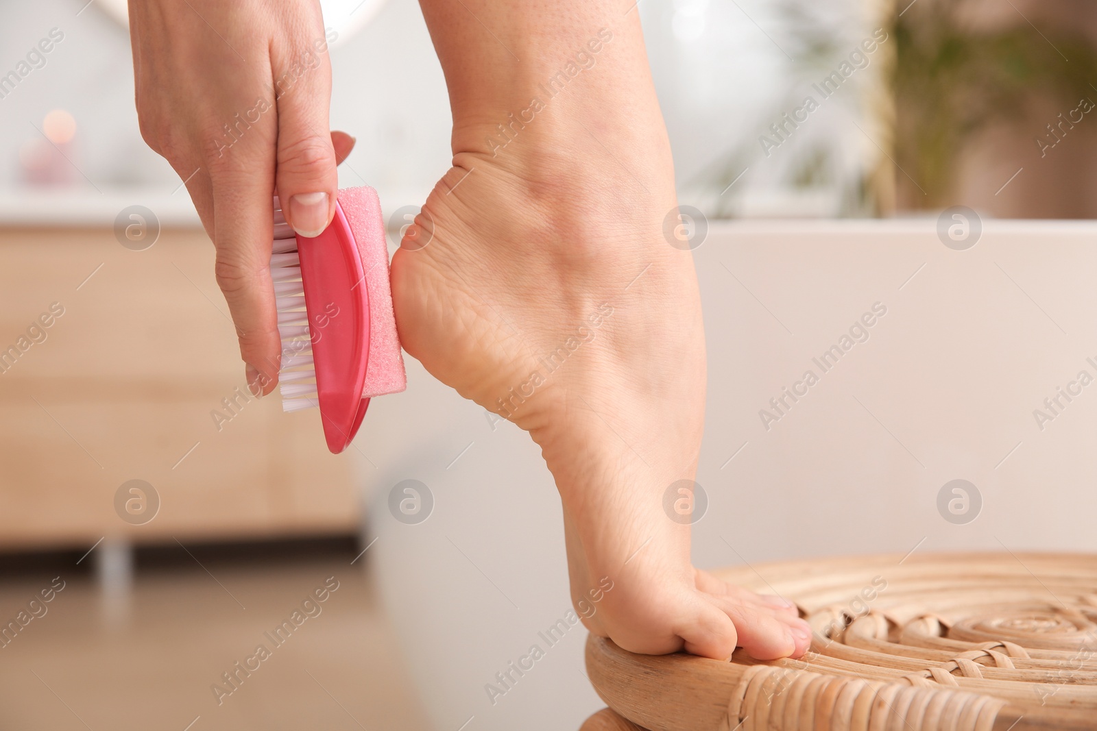 Photo of Woman using pumice stone for removing dead skin from feet in bathroom, closeup