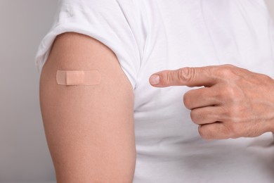 Photo of Man pointing at adhesive bandage after vaccination on light grey background, closeup
