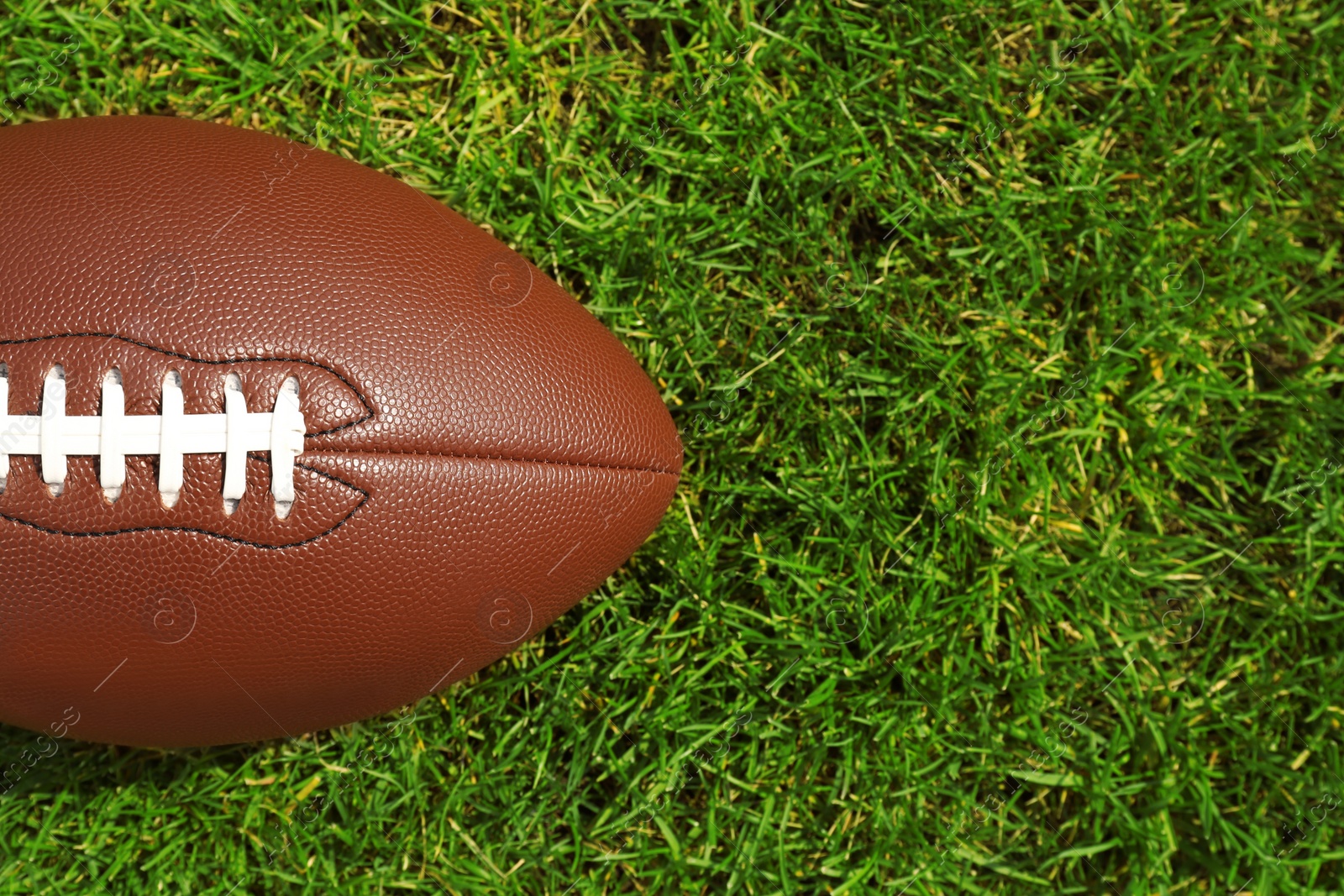 Photo of American football ball on green grass, top view. Space for text