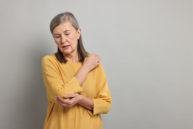 Photo of Arthritis symptoms. Woman suffering from pain in elbow on gray background, space for text