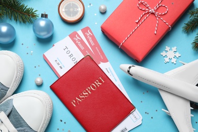 Photo of Flat lay composition with Christmas decorations, passport and airline tickets on light blue background. Winter vacation