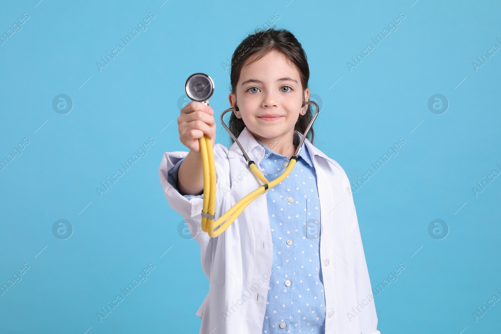 Photo of Little girl with stethoscope dressed as doctor on light blue background. Pediatrician practice