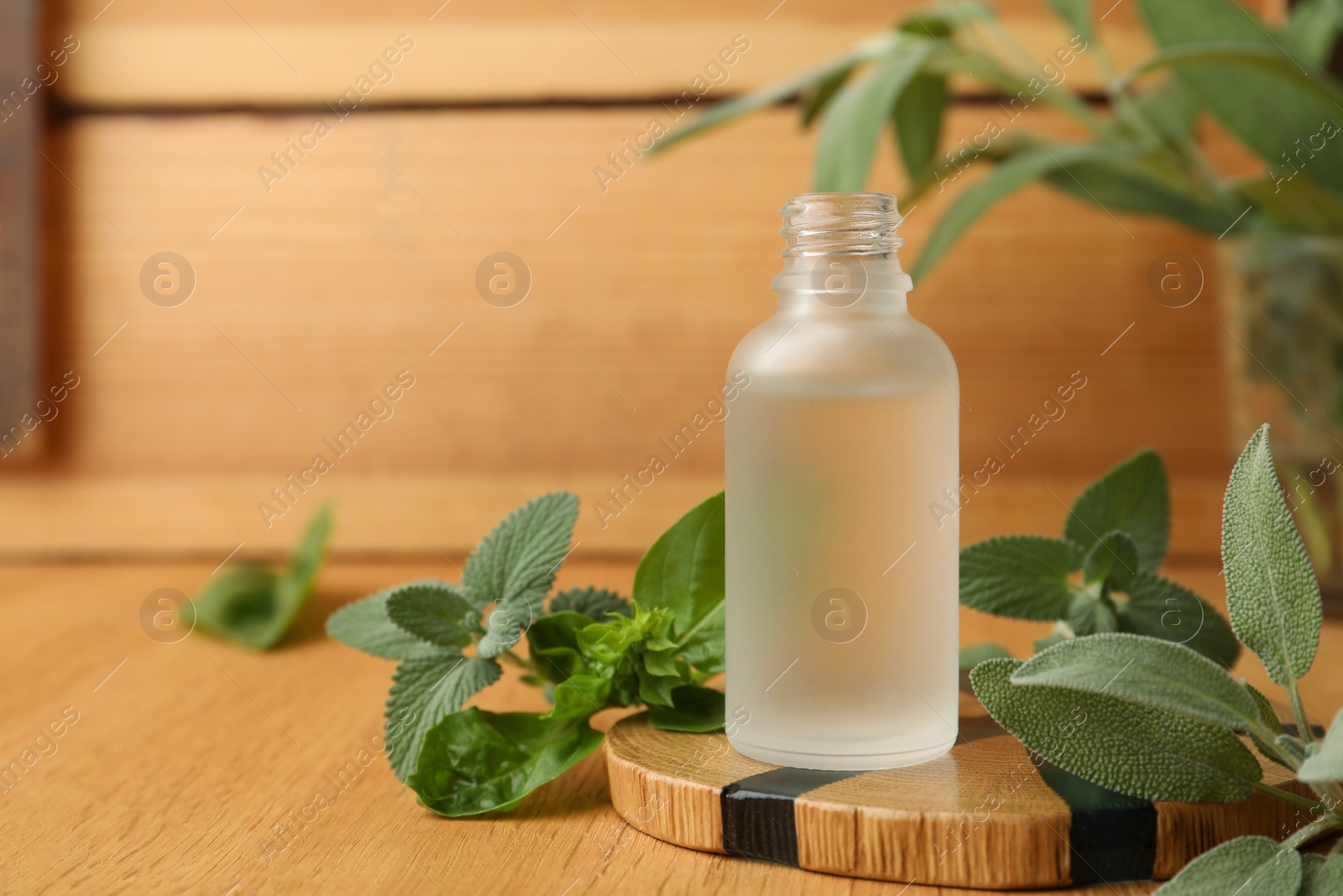 Photo of Bottle of essential oil and fresh herbs on wooden table, space for text