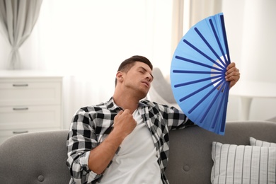 Man with hand fan sitting on sofa. Summer season