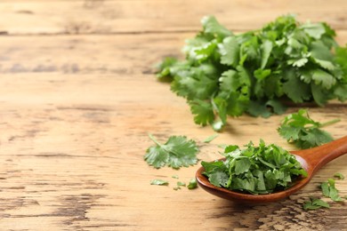 Photo of Fresh green cilantro and spoon on wooden table. Space for text
