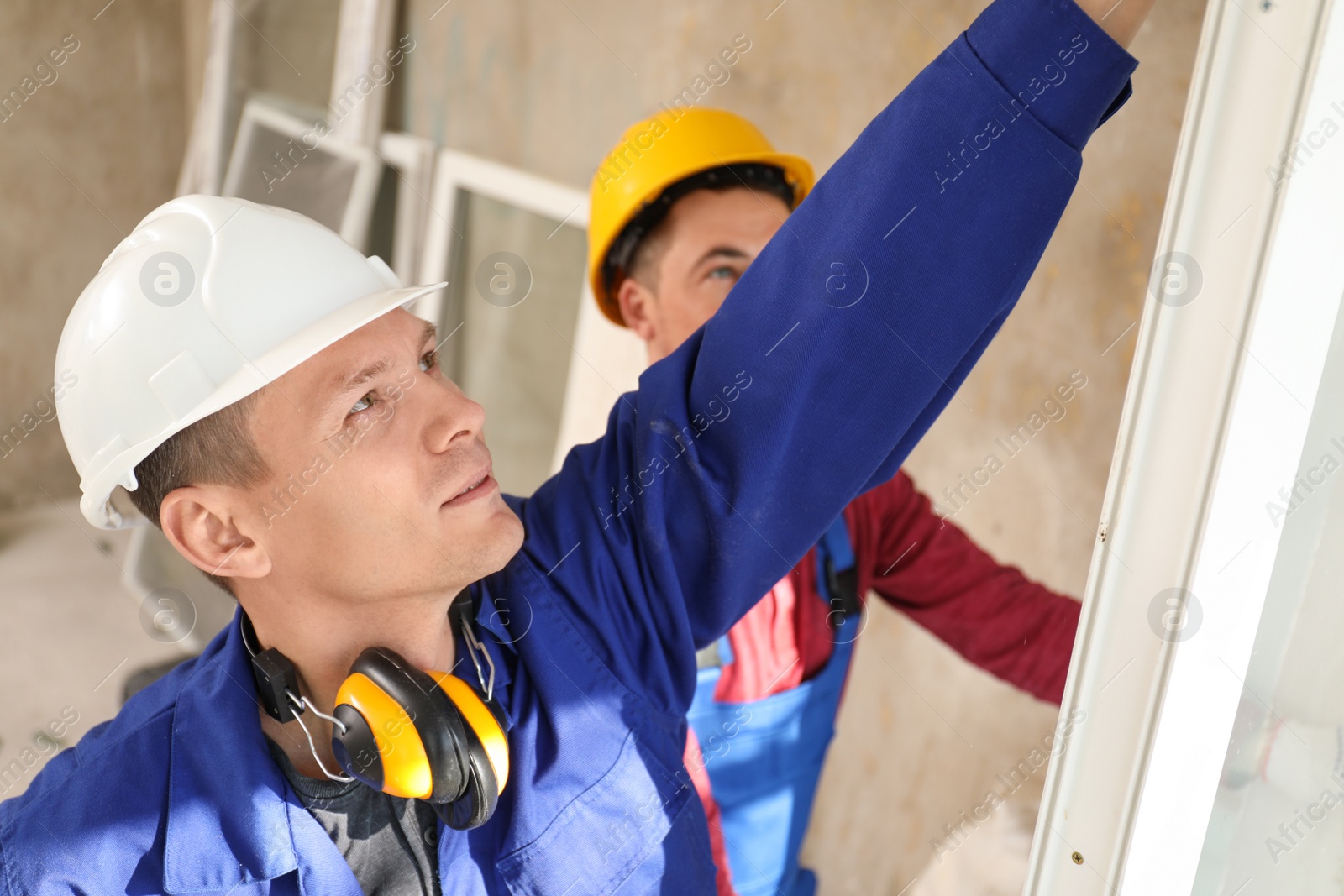 Photo of Workers in uniform installing plastic window indoors