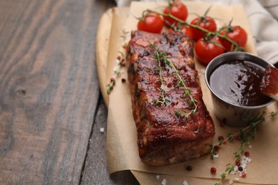 Photo of Tasty roasted pork ribs served with thyme, sauce and tomatoes on wooden table, closeup. Space for text