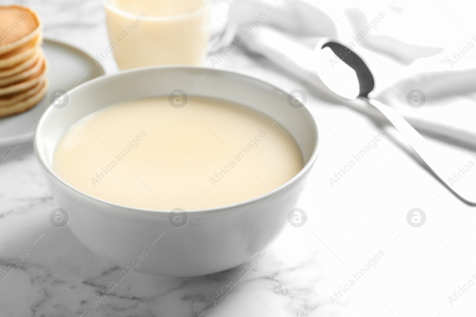 Photo of Bowl with condensed milk on marble table, space for text. Dairy products