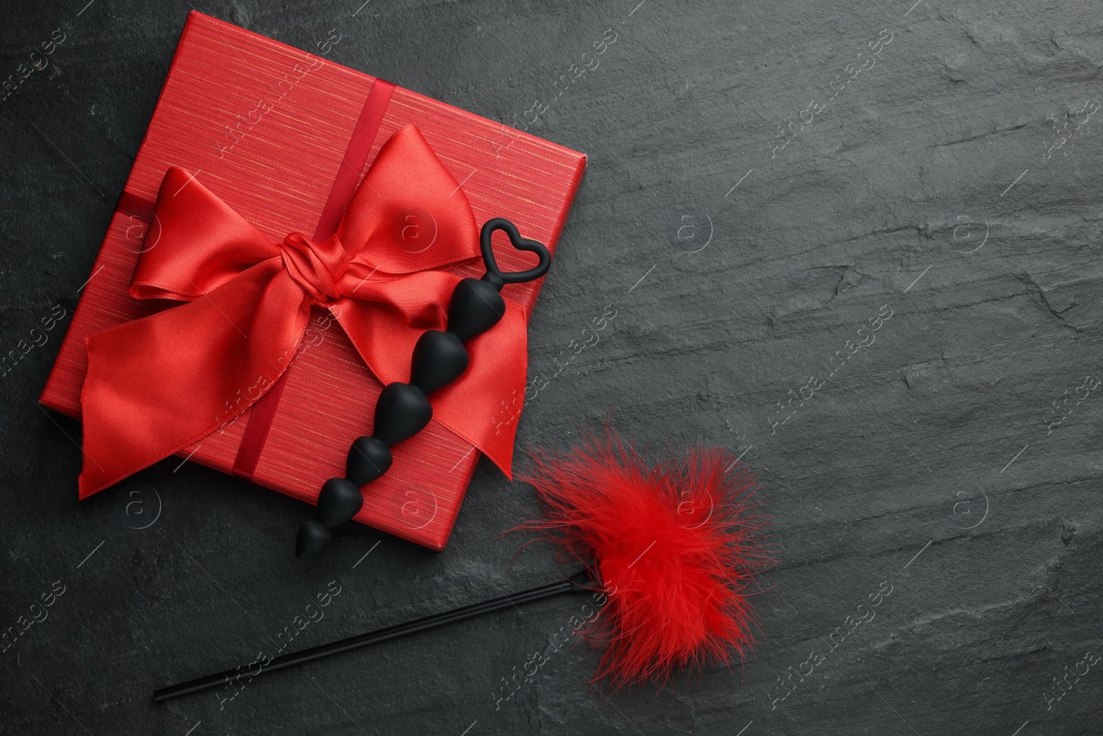 Photo of Anal beads, red feather tickler and gift box on black table, flat lay with space for text. Sex toys