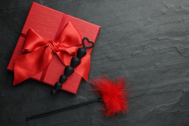 Photo of Anal beads, red feather tickler and gift box on black table, flat lay with space for text. Sex toys