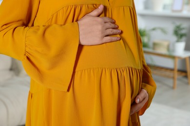 Photo of Pregnant woman touching belly in living room, closeup