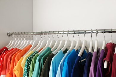 Hangers with different colorful clothes on rack in wardrobe