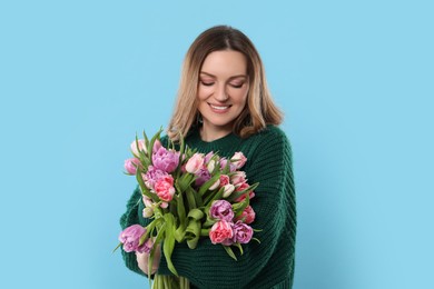 Happy young woman with bouquet of beautiful tulips on light blue background