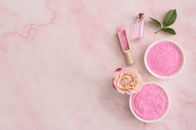 Bowls and scoop with sea salt, beautiful rose on pink marble table, flat lay. Space for text