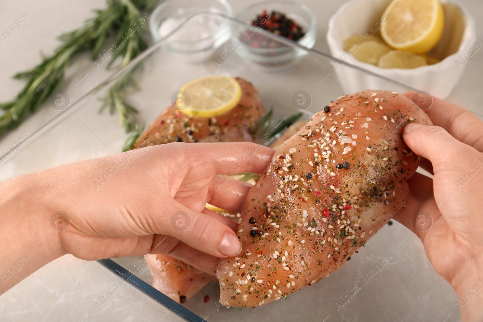 Photo of Woman cooking chicken breasts with lemon at grey marble table, closeup