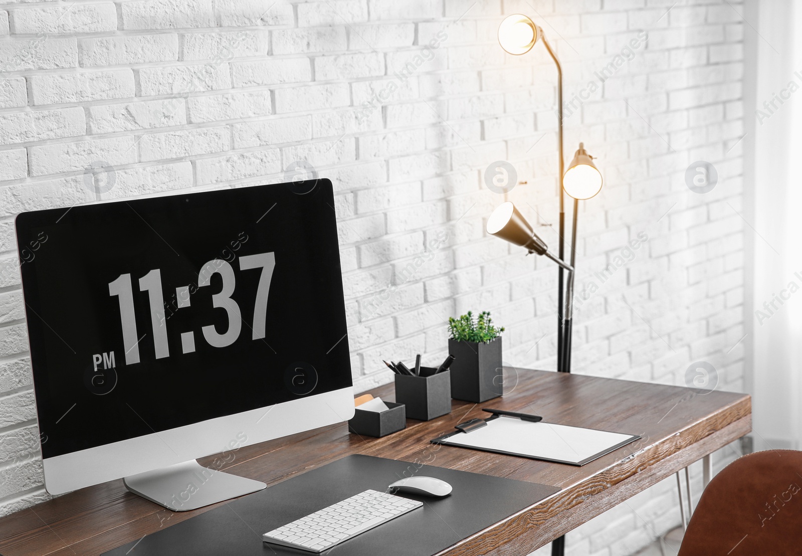 Photo of Modern workplace interior with computer on table near brick wall