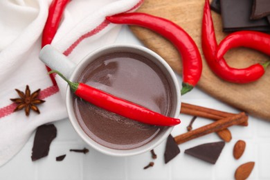 Cup of hot chocolate with chili pepper on white tiled table, flat lay