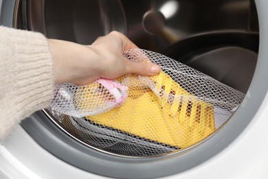 Photo of Woman putting stylish sneakers into washing machine, closeup