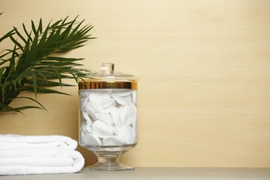 Composition of glass jar with cotton pads on table near light wooden wall. Space for text