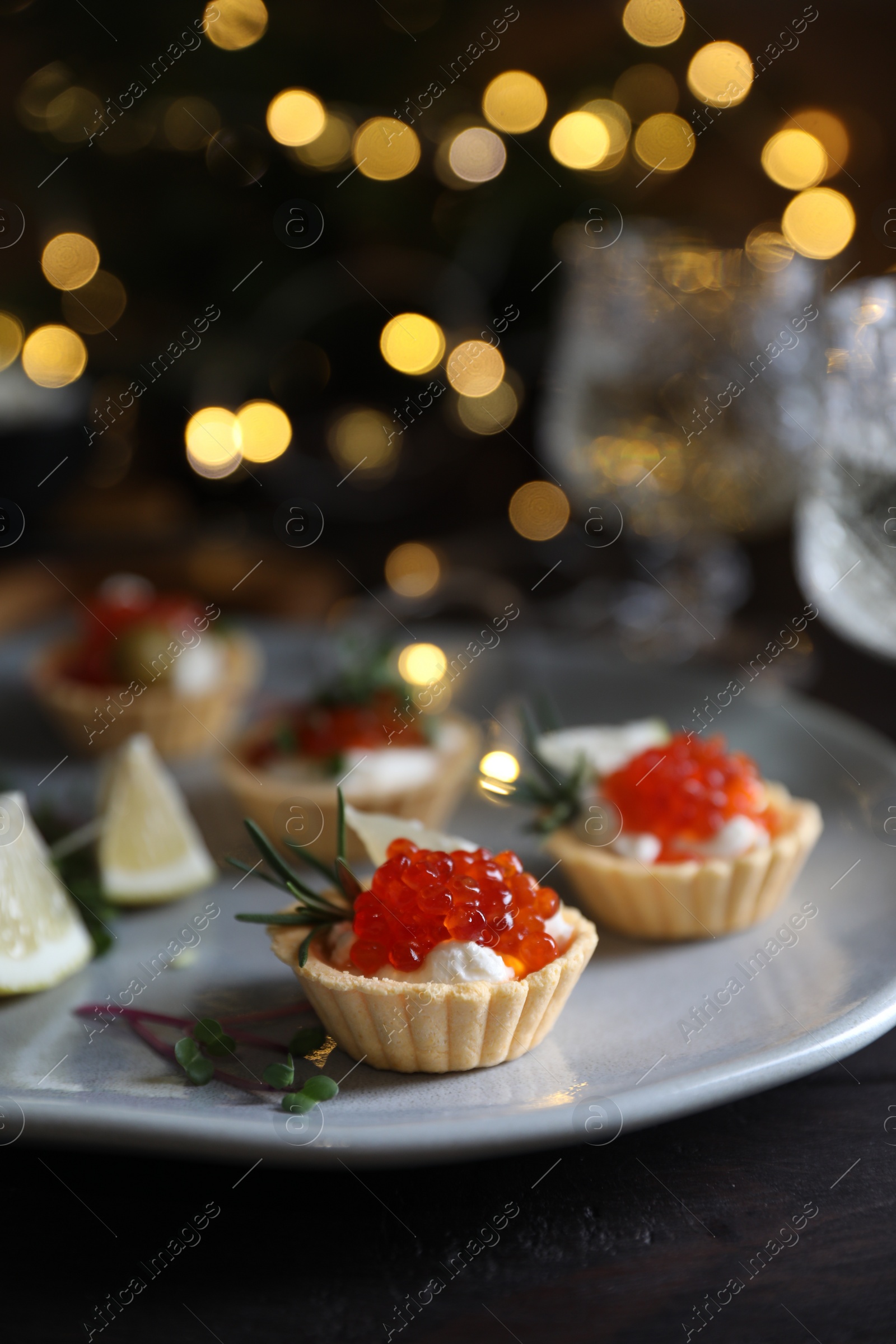 Photo of Delicious tartlets with red caviar, cream cheese and lemon served near wine on black table, closeup. Space for text