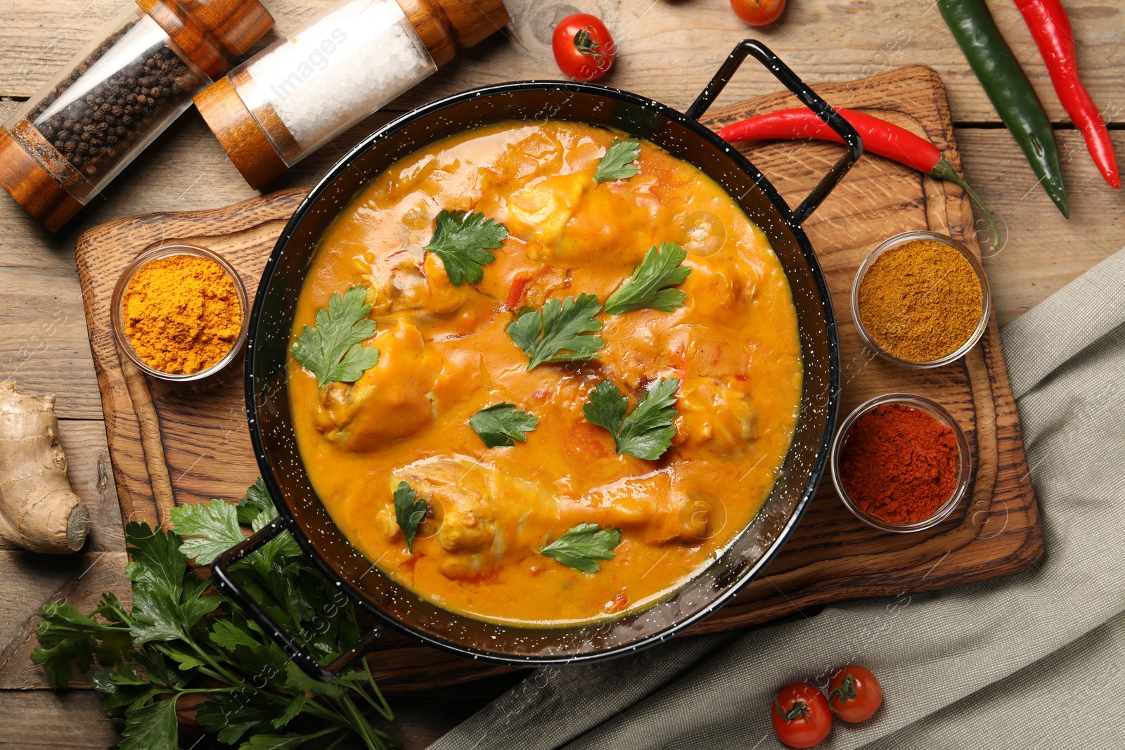 Photo of Tasty chicken curry with parsley and ingredients on wooden table, flat lay