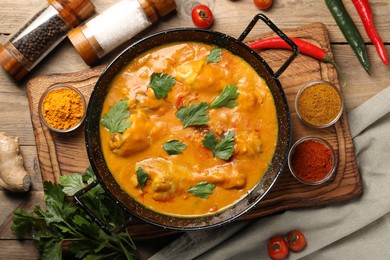 Tasty chicken curry with parsley and ingredients on wooden table, flat lay