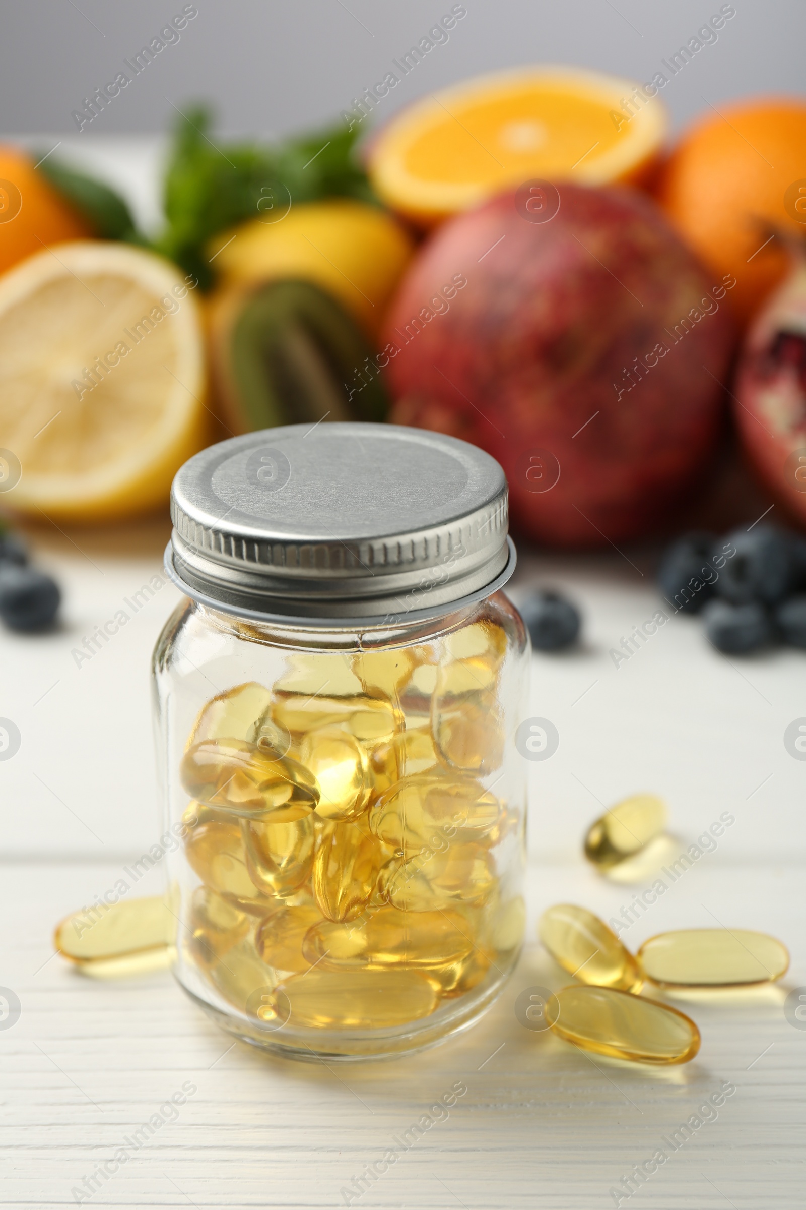 Photo of Vitamin pills in bottle and fresh fruits on white wooden table