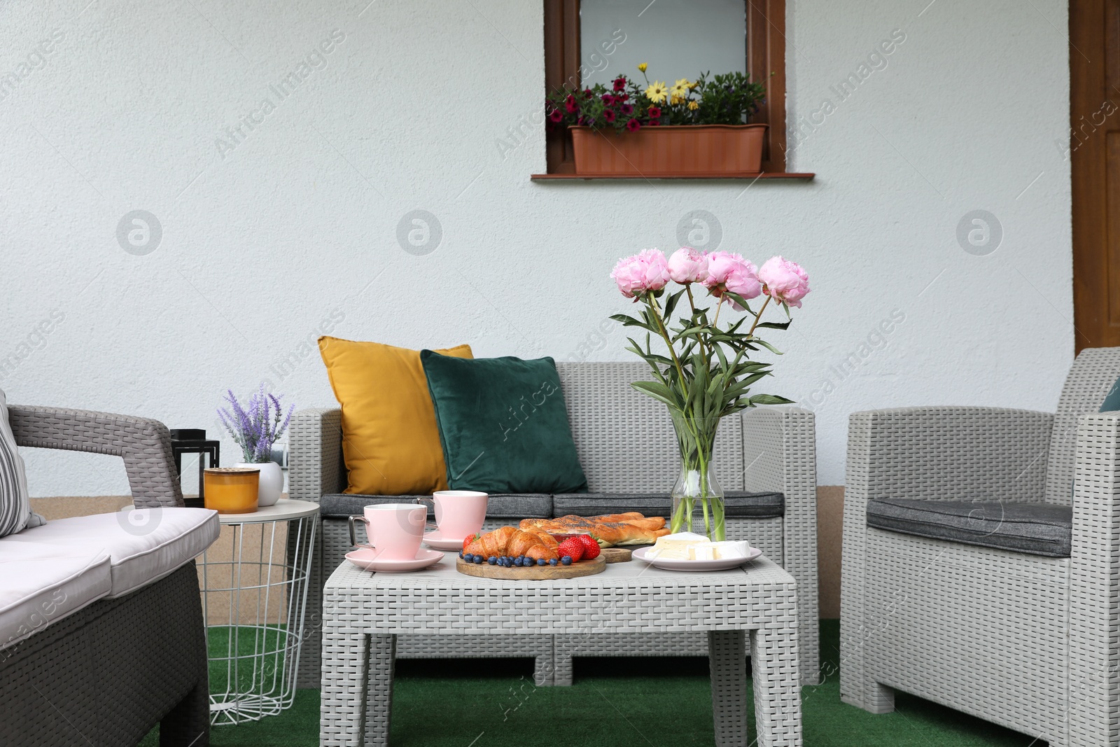 Photo of Morning drink, pastry, berries, cheese and vase with flowers on rattan table. Summer breakfast on terrace