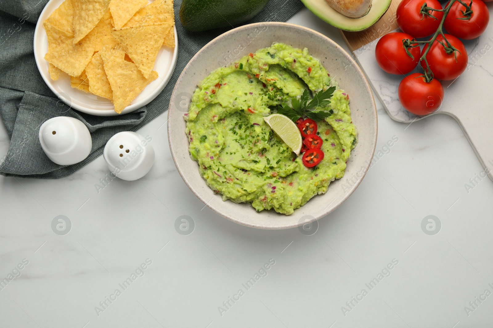 Photo of Delicious guacamole with nachos chips and ingredients on white marble table, flat lay. Space for text