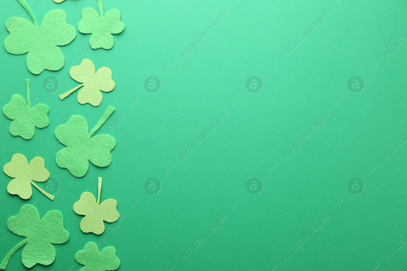 Photo of St. Patrick's day. Decorative clover leaves on green background, flat lay. Space for text