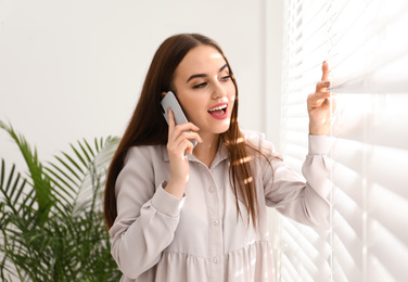 Photo of Beautiful woman talking on mobile phone near window indoors