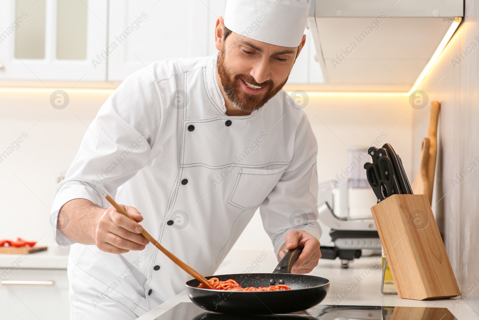 Photo of Professional chef cooking delicious spaghetti in frying pan indoors