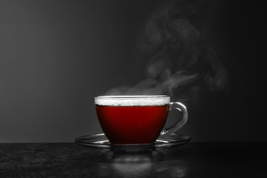 Photo of Glass cup of hot tea on stone table against grey background, space for text