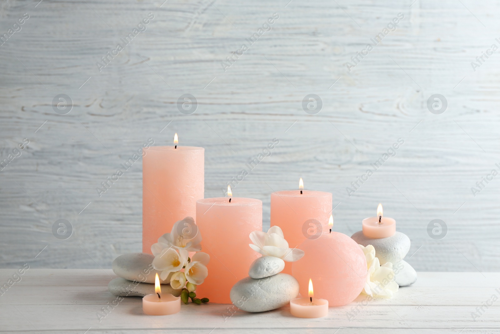 Photo of Composition of burning candles, spa stones and flowers on table. Space for text