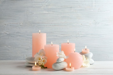 Photo of Composition of burning candles, spa stones and flowers on table. Space for text