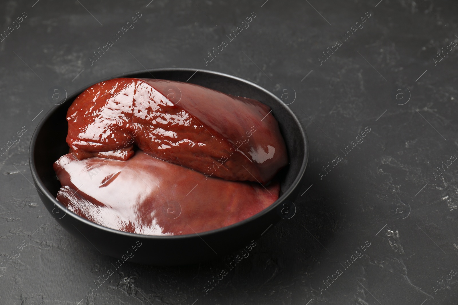 Photo of Pieces of raw beef liver in bowl on black table, closeup. Space for text