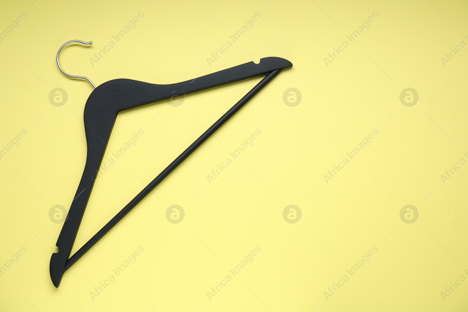 Photo of Empty black hanger on yellow background, top view. Space for text