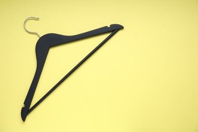 Empty black hanger on yellow background, top view. Space for text