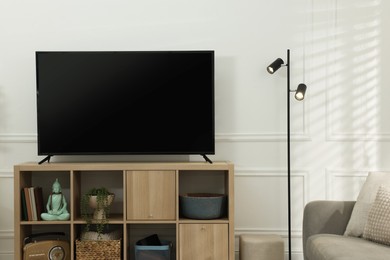 Photo of Modern TV on cabinet and lamp near white wall indoors. Interior design