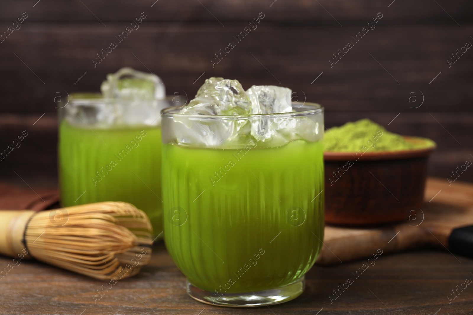 Photo of Glass of delicious iced green matcha tea and bamboo whisk on wooden table, closeup