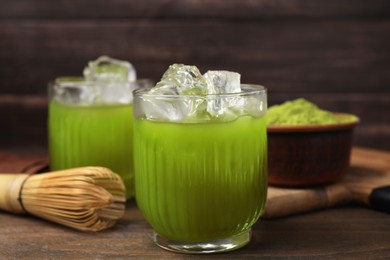 Photo of Glass of delicious iced green matcha tea and bamboo whisk on wooden table, closeup