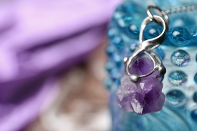 Photo of Beautiful silver pendent with amethyst gemstone on glass stand against blurred background. Space for text