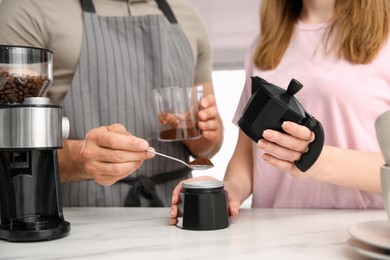 Photo of Couple making coffee together in kitchen, man putting ground beans into moka pot