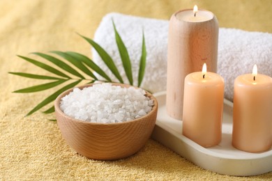 Spa composition. Burning candles, sea salt and towel on soft yellow fabric