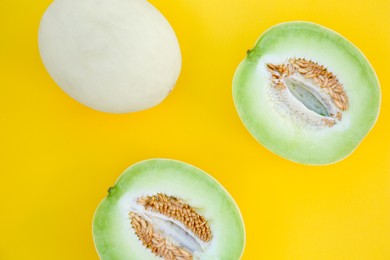 Whole and cut fresh ripe honeydew melons on yellow background, flat lay