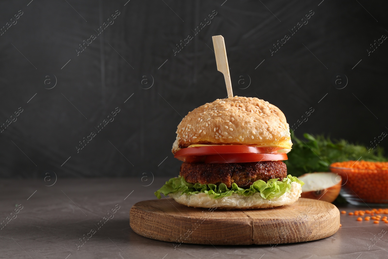 Photo of Board with delicious vegetarian burger on grey textured table. Space for text